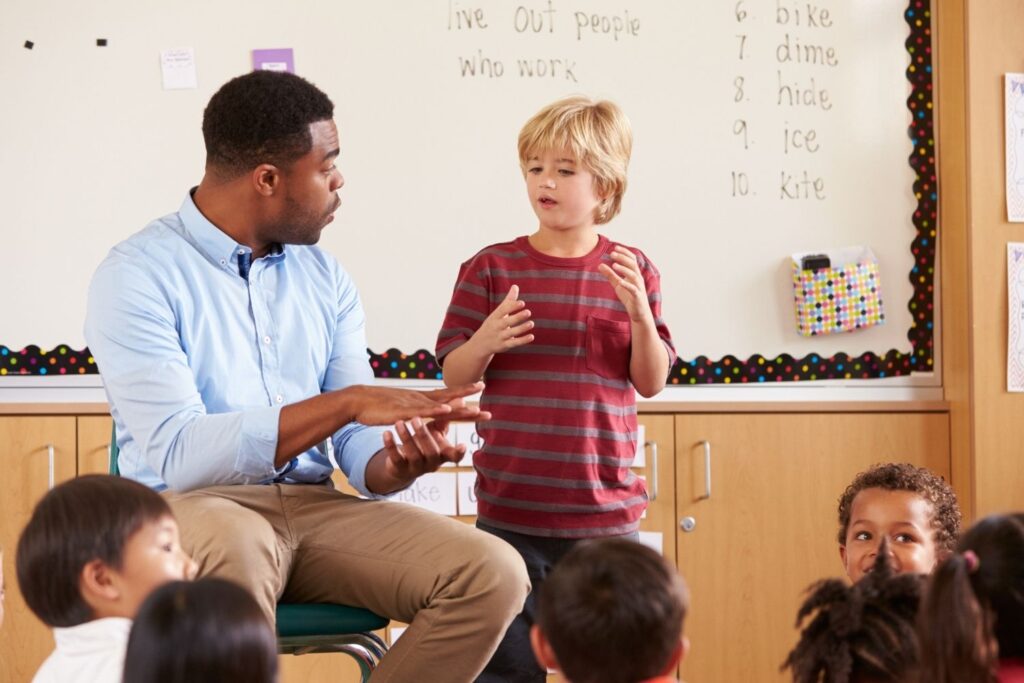 Presenting to the class Young boy giving a presentation standing at the front of his class with his teacher