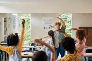 A group of students dance with a teacher in a classroom.