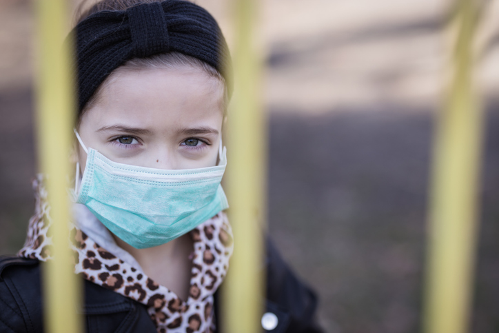 Little girl looking through a fence Girl wearing a mask because of the pandemic.