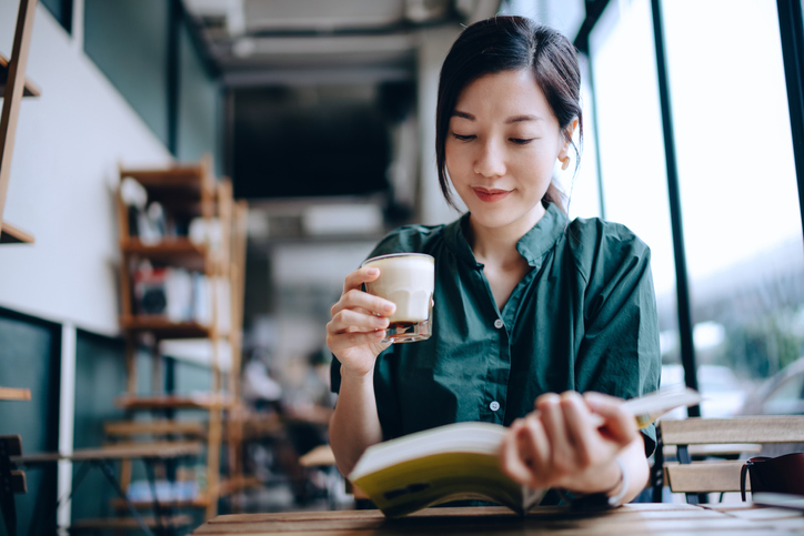 Young Asian woman taking a break, having a quiet time enjoying a cup of coffee and reading book in cafe Teacher reading a book in a coffee shop
