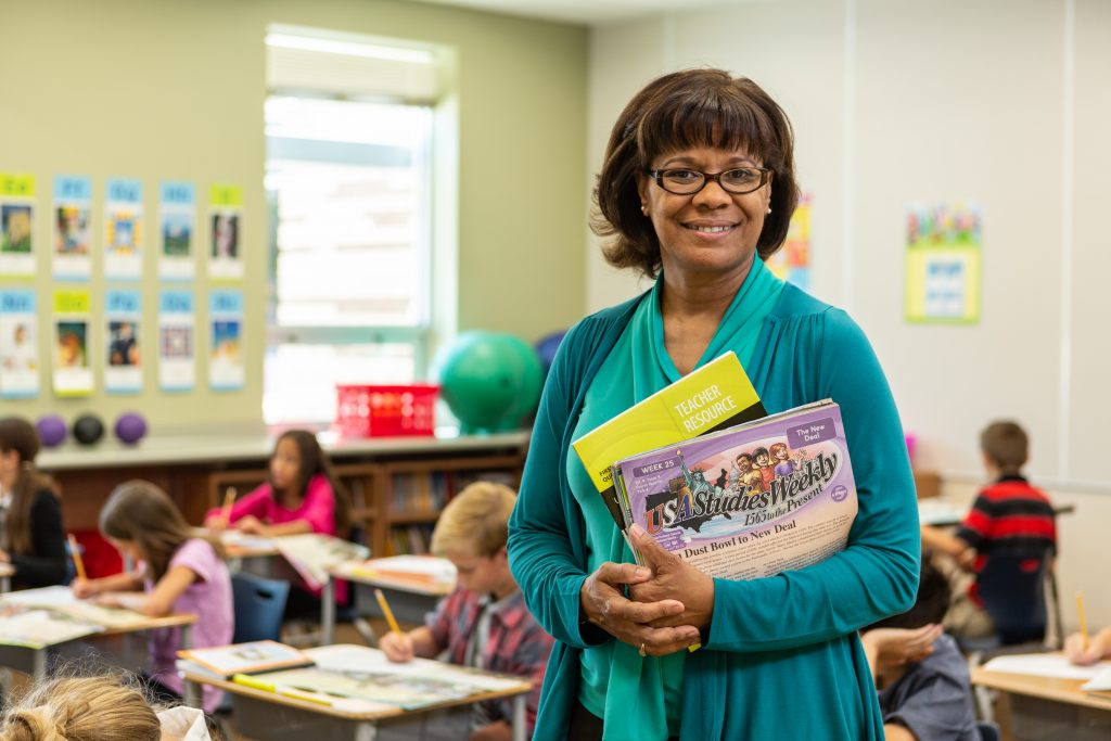 2018 Studies Weekly Photoshoot | Female teacher holding book, workbook. Curriculum-based Professional Development Helps Teachers Use Studies Weekly Effectively