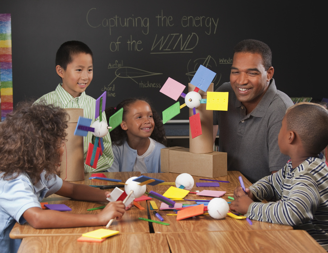 Teacher and children making paper wind turbines in classroom Science teacher doing a wind experiment with students