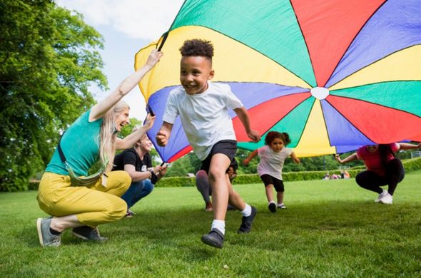 Children running and playing with a big, rainbow parachute