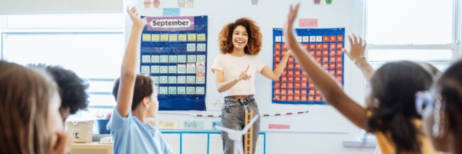 Smiling teacher engaging with enthusiastic diverse elementary students raising their hands in a bright, colorful classroom setting. Smiling teacher engaging with enthusiastic diverse elementary students raising their hands in a bright, colorful classroom setting.