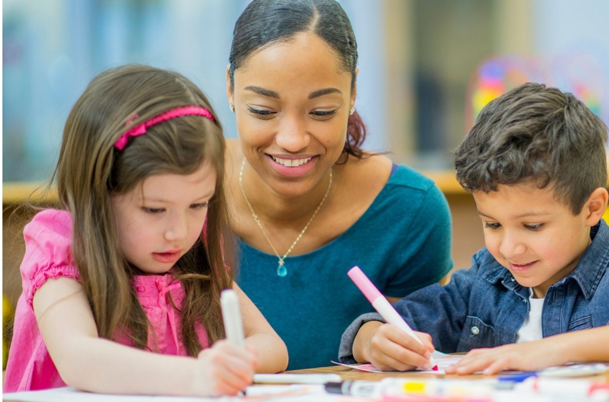 Teacher sitting with students as they draw