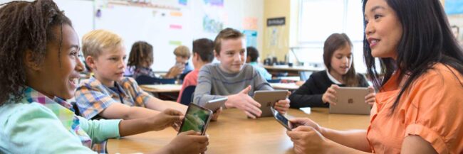 Teaching sitting at round table with several elementary students
