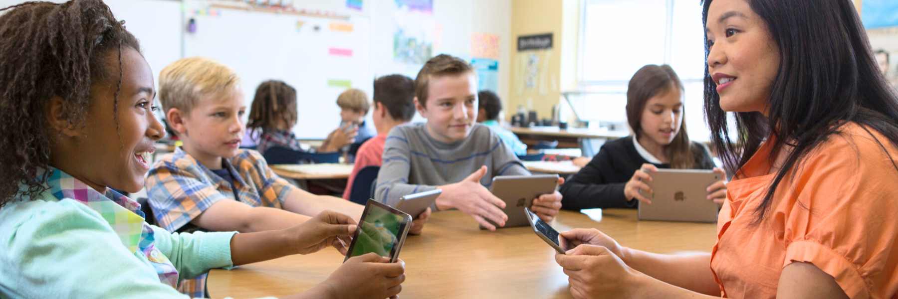 Students and teacher working together Teaching sitting at round table with several elementary students