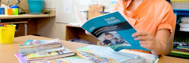 Teacher sitting at a desk unboxing teacher edition and student edition