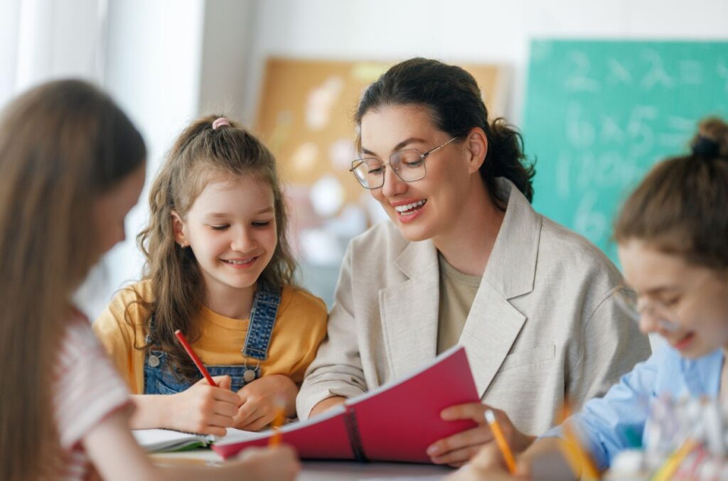 Teacher reading to students Teacher sitting at a desk reading a book to a student