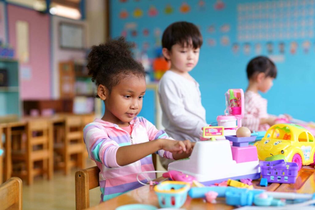 Little girl playing with a toy cash register in preschool