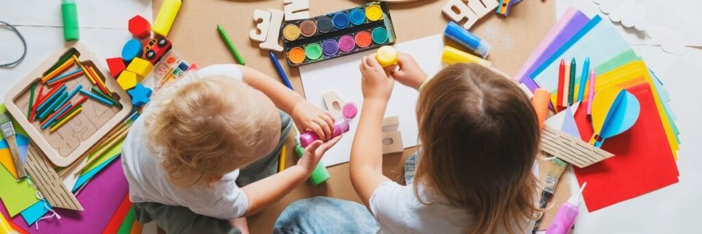 Two preschool children painting and sitting around arts and crafts supplies