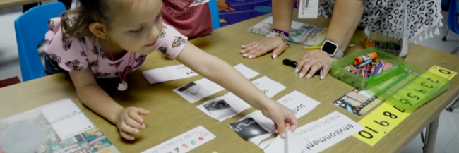 Elementary student using school desk student reaching over desk for Studies Weekly materials
