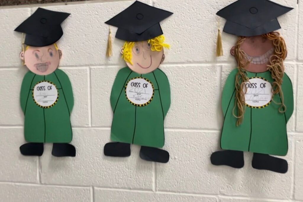 Paper cutouts of students with graduation caps and yarn hair for a student art project