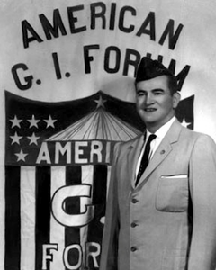 Hector P. Garcia, a Hispanic doctor, civil rights advocote, and founder of the American G.I. Force, standing in front of an American G.I. Forum banner.